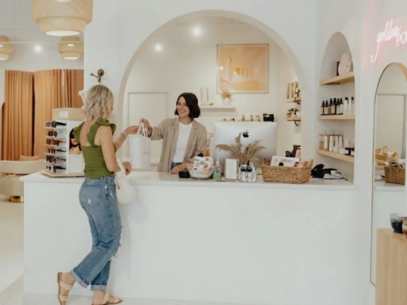 A sales associate handing a bag back across the counter to a customer in a bright clothing store