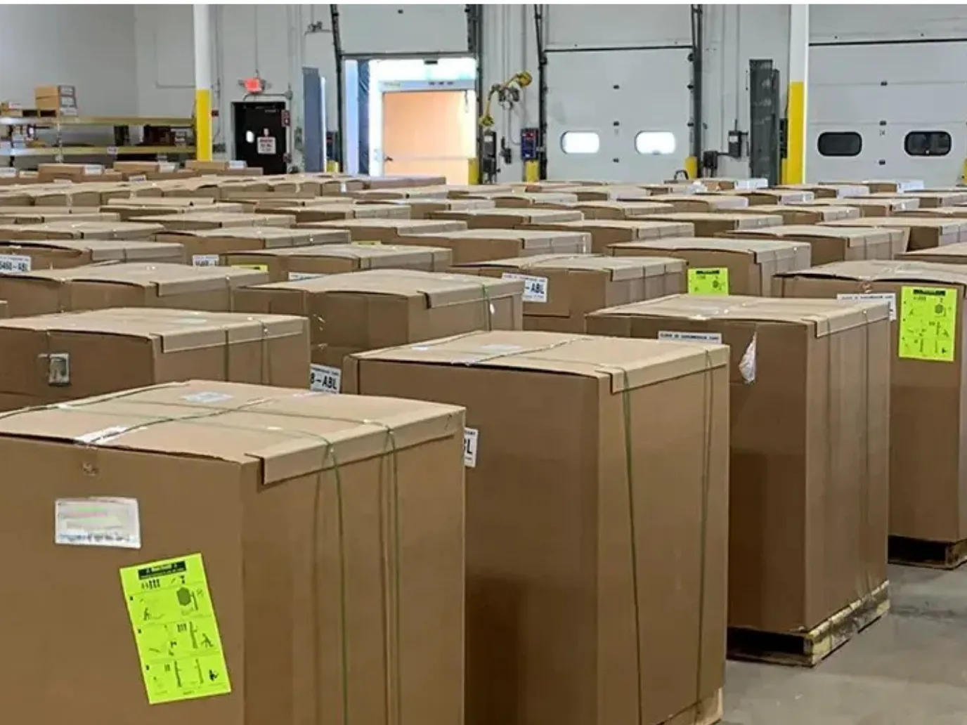 Rows of strapped and labelled pallets waiting on a warehouse floor beside an open loading dock